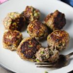 Healthy Meatballs with Zucchini & Lean Beef on a plate with fork cutting into one and pan in background. They're loaded with flavor from the garlic, minced onion, salt, and pepper.  The zucchini brings moisture, texture, and bulks up the meatballs with healthiness.