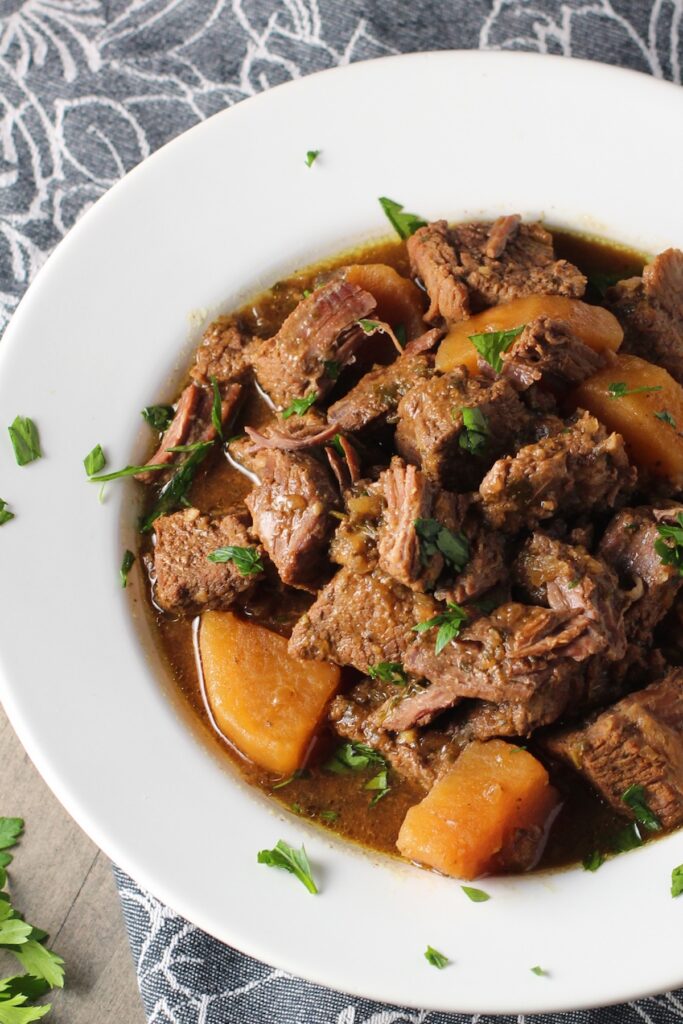 Slow Cooker Honey Garlic Beef and Potatoes in a bowl with parsley on top.  It's a delicious easy dinner with tender beef cubes are cooked in the slow cooker with lots of delicious garlic, onions, and potatoes.  Then honey and molasses are added for that touch of sweet.