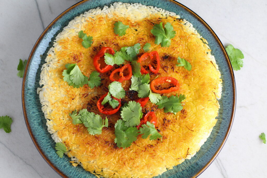 Saffron Butter Crispy Rice on a plate with cilantro and peppadew peppers on top. Saffron brings a floral note and beautiful yellow-orange color.  Added to the butter is what gives this crispy rice the buttery, crispy bottom.