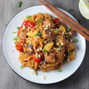 Thai vegetable stir fry with tofu and noodles on a plate with chopsticks.