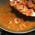 Adding cooked cajun shrimp and sausage back to sauce in a pan for Shrimp and Grits recipe.