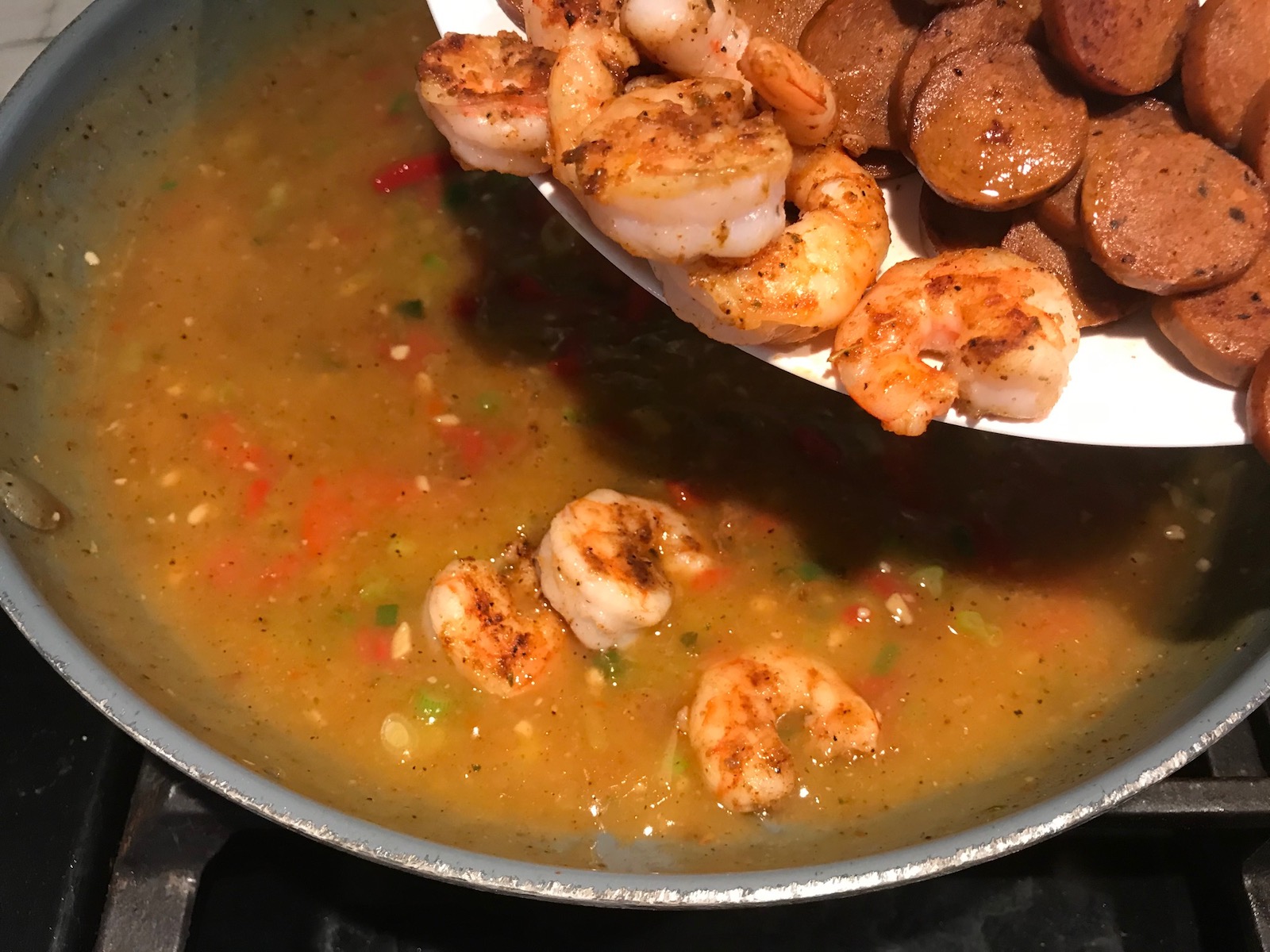 Adding cooked cajun shrimp and sausage back to sauce in a pan for Shrimp and Grits recipe. 