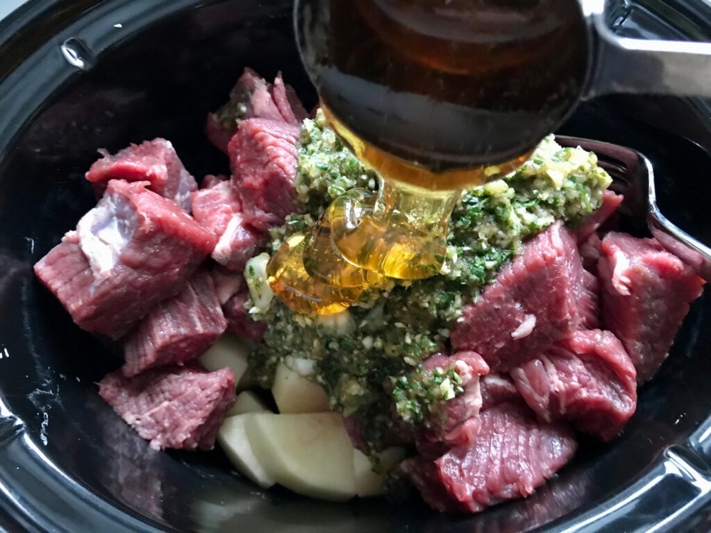 Pouring honey over raw beef and other ingredients in slow cooker for Honey Garlic Beef and Potatoes. It's a delicious easy dinner made in the slow cooker with tender beef cubes are cooked in the slow cooker with lots of delicious garlic, onions, and potatoes.  Then honey and molasses are added for that touch of sweet.