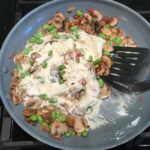 Spatula mixing Ricotta, Bacon, Mushroom Sauce in pan on stove. It's creamy, rich, decadent, comforting, and downright delicious!