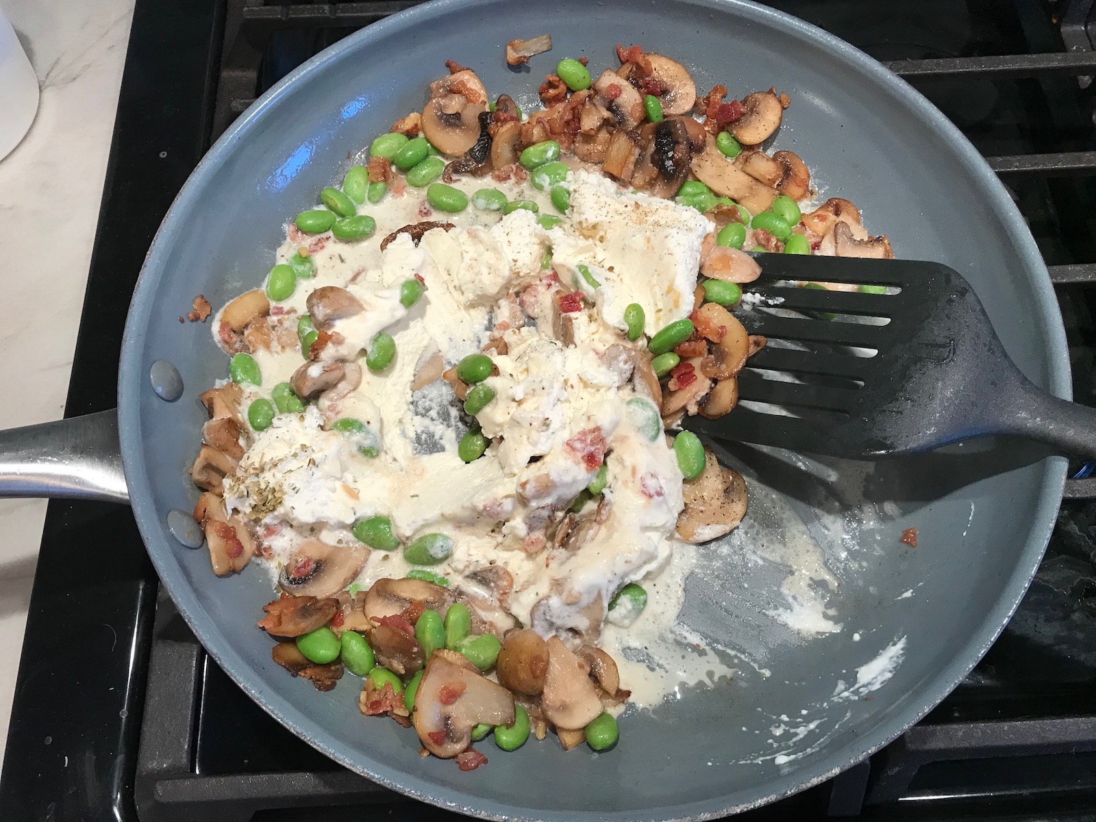 Spatula mixing Ricotta sauce with Bacon, Mushroom Sauce in pan on stove. It's creamy, rich, decadent, comforting, and downright delicious!