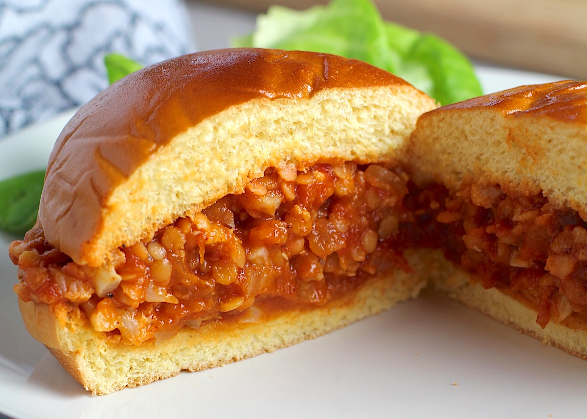 Vegetarian Sloppy Joes sandwich overstuffed with cauliflower and lentils filling in a brioche bun on a plate cut in half and facing out to see the center.