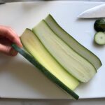 Hand holding slice of zucchini on a cutting board for White Lasagna Recipe with Zucchini and Ground Beef