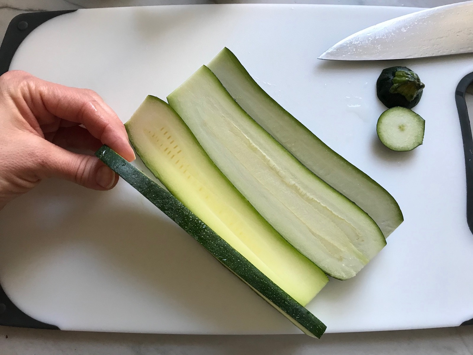 Hand holding slice of zucchini on a cutting board for White Lasagna Recipe with Zucchini and Ground Beef