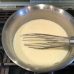 Whisk mixing white sauce in a pot for White Lasagna Recipe with Zucchini and Ground Beef