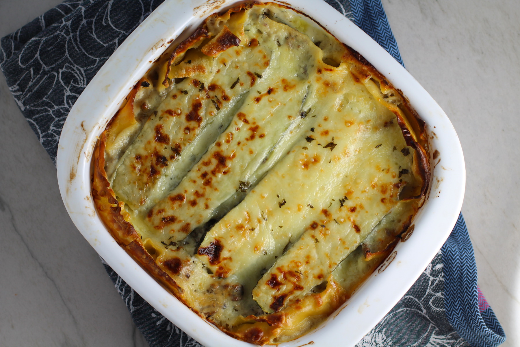 White Lasagna Recipe with Zucchini and Ground Beef with browned melted cheese on top in casserole dish! It's a make-ahead family dinner! It's creamy, hearty, and delicious with layers of noodles, zucchini, ground beef, creamy cheese, and a silky white sauce. 