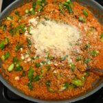 Parmesan cheese added to Asparagus and Tomato Quinoa Risotto in a pan.