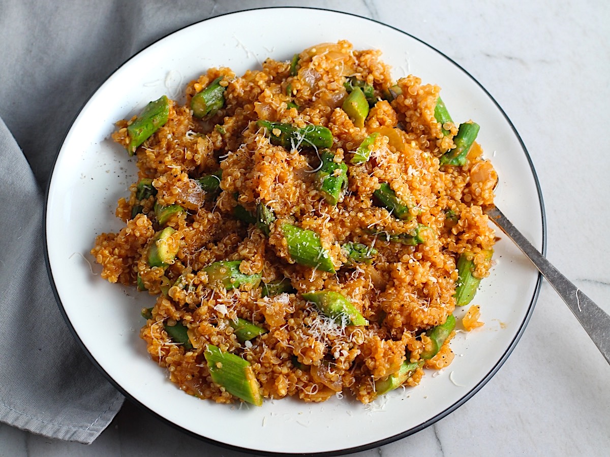 Asparagus and Tomato Quinoa Risotto with parmesan on top on a plate with fork.