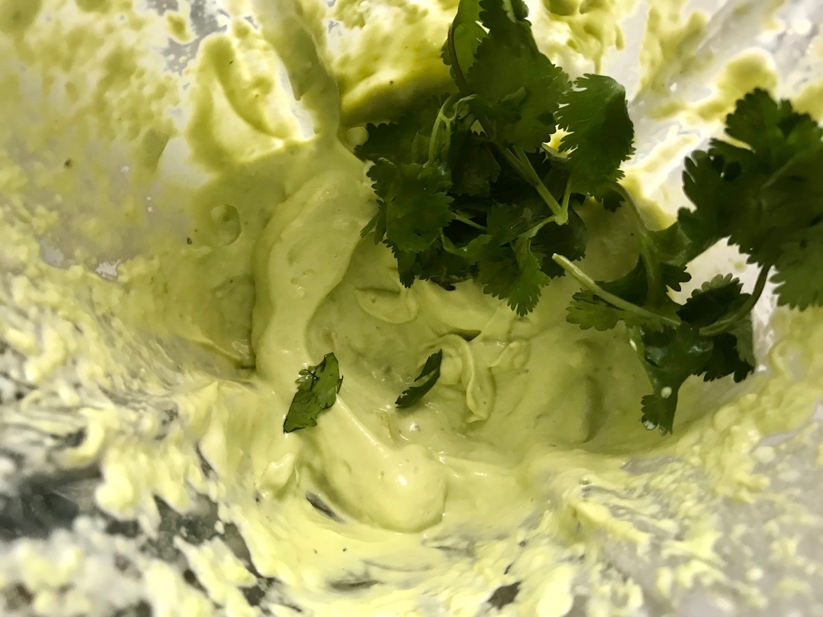 Fresh cilantro leaves added on top of blended Avocado in a blender for Avocado Crema Recipe. It goes on everything! It's a creamy, tangy, rich and delicious sauce that's made in just minutes in the blender!