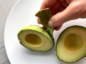 Hand peeling the skin from avocado half for Avocado Crema recipe.