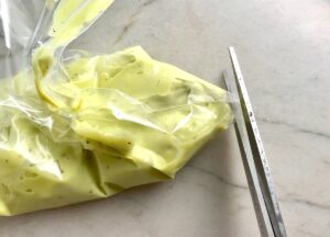 Scissors snipping corner off of a baggie filled with Avocado Crema Recipe. It goes on everything! It's a creamy, tangy, rich and delicious sauce that's made in just minutes in the blender!