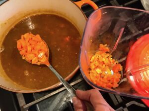 Spoon transfering carrots from pot to blender for Golden Carrot Ginger Soup Recipe. 