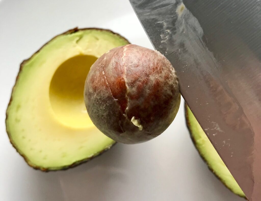 Knife pulling pit from avocado half for Taco Quinoa Bowls with Ground Beef, corn, cotija, tomatoes, and cilantro lime crema.