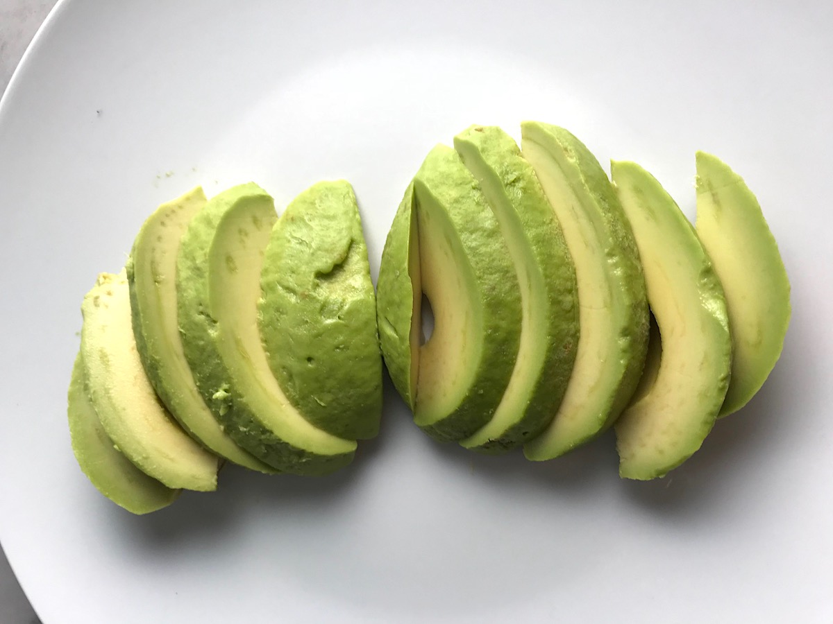 Peeled and sliced avocado fanned out on a plate for Taco Quinoa Bowls with Ground Beef, corn, cotija, tomatoes, and cilantro lime crema.