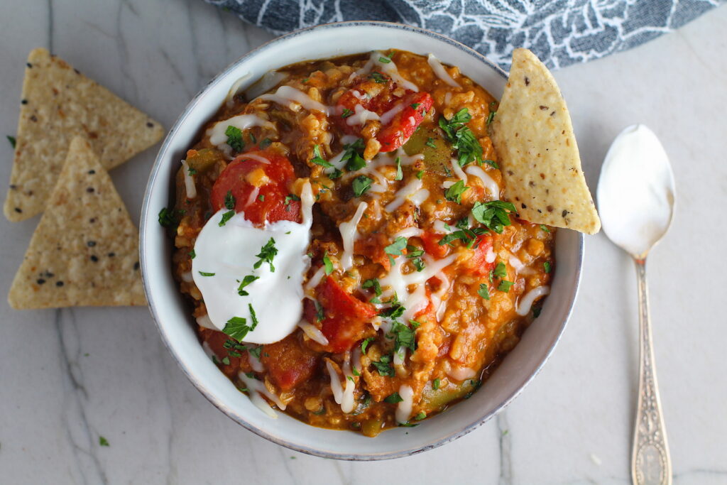 Bowl of Tex Mex Unstuffed Peppers with Ground Chicken with a dollop of sour cream and a tortilla chip dipped in.  Juicy Sweet Bell Peppers are chopped up and cooked with the Tex Mex style ground chicken, tomatoes, Mexican seasonings, cheese, rice and corn tortillas.