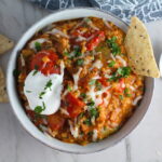 Bowl of Tex Mex Unstuffed Peppers with Ground Chicken with a dollop of sour cream and a tortilla chip dipped in.  Juicy Sweet Bell Peppers are chopped up and cooked with the Tex Mex style ground chicken, tomatoes, Mexican seasonings, cheese, rice and corn tortillas.