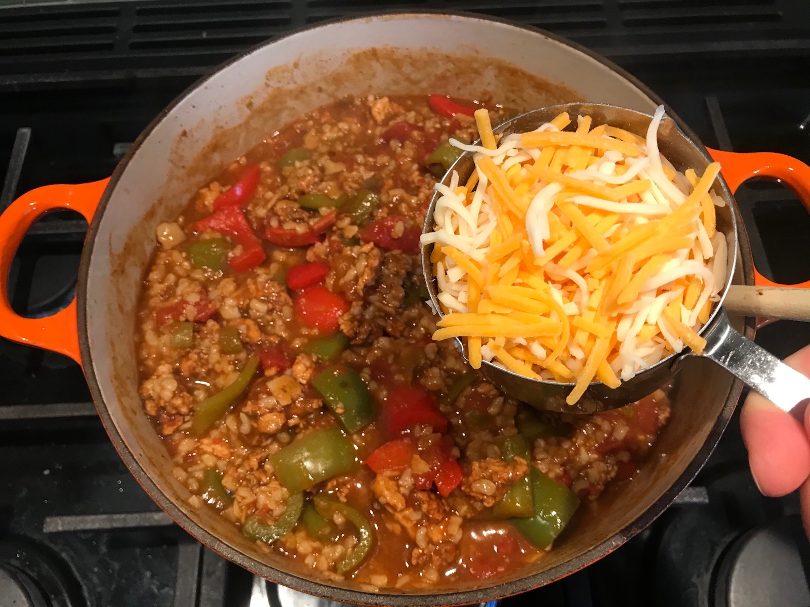 Adding shredded cheese to pot of cooked Tex Mex Unstuffed Peppers with Ground Chicken.  Juicy Sweet Bell Peppers are chopped up and cooked with the Tex Mex style ground chicken, tomatoes, Mexican seasonings, cheese, rice and corn tortillas.