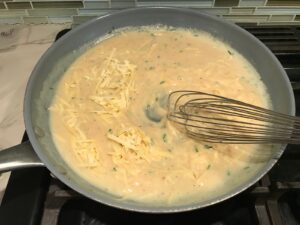 Whisk mixing shredded gruyere cheese into sauce in large frying pan for Velvety Barley Recipe with Bacon and Gruyere Cheese.  It's creamy, rich, nutty, smokey, hearty, and utterly delicious.