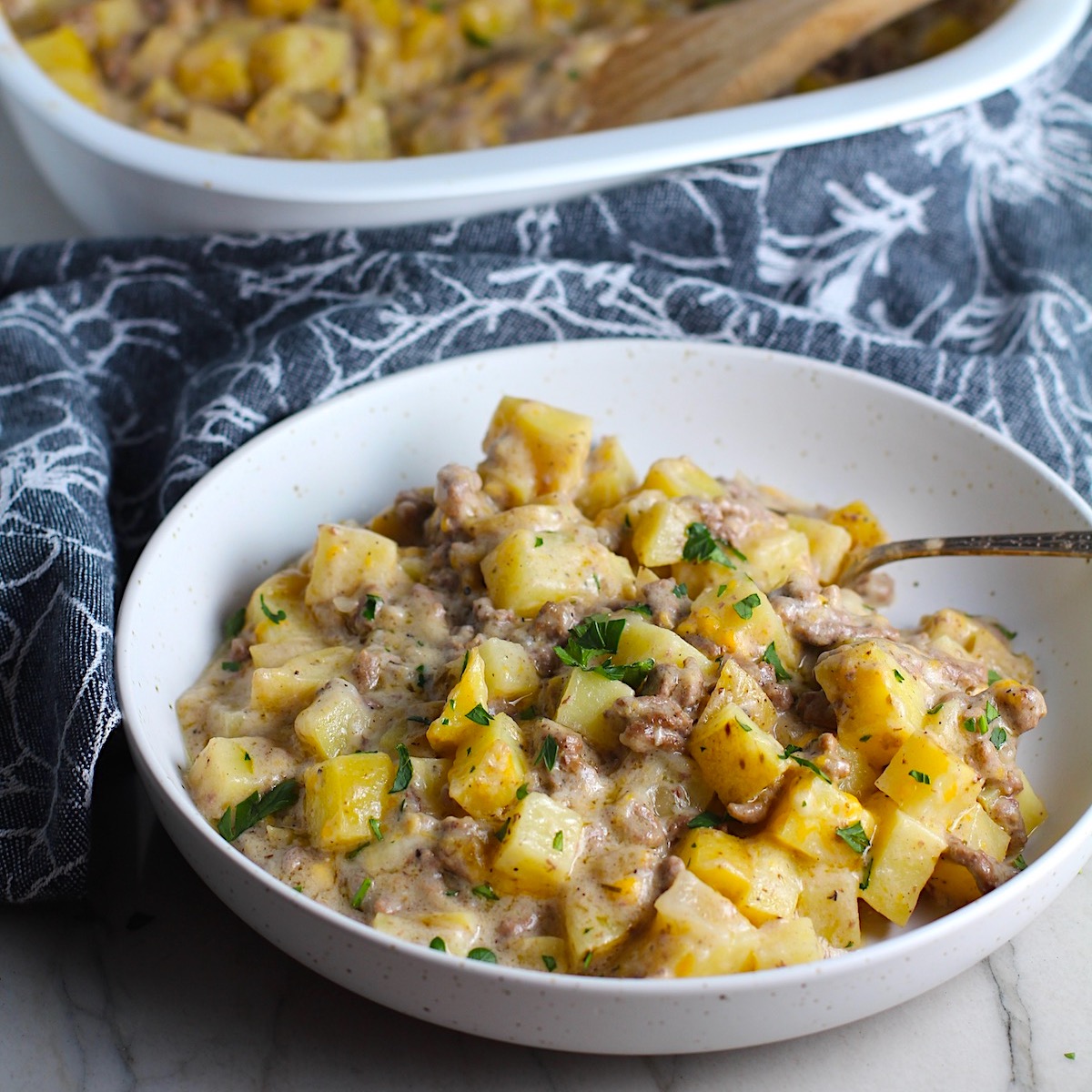 Cheesy Hamburger Potato Casserole in a bowl with a spoon. It's an easy, yummy, and cozy weeknight family dinner. 