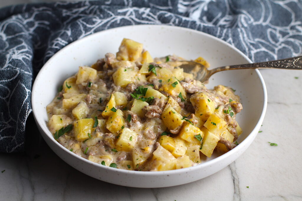 Cheesy Hamburger Potato Casserole in a bowl with a spoon. It's an easy, yummy, and cozy weeknight family dinner. 