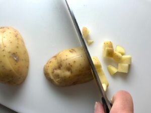 Knife dicing raw yukon gold potato with skin on for Cheesy Hamburger Potato Casserole. It's an easy, yummy, and cozy weeknight family dinner. 