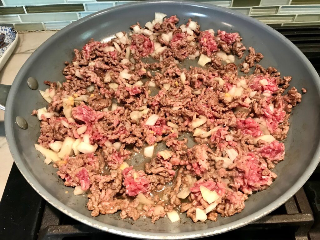 Ground beef and onions cooking in a pan for Cheesy Hamburger Potato Casserole. It's an easy, yummy, and cozy weeknight family dinner. 