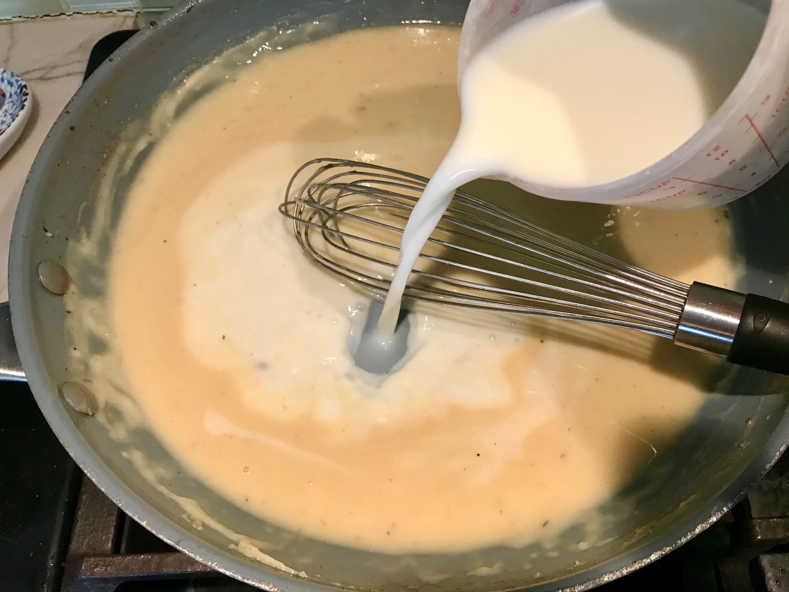 Whisking the milk into the sauce in the pan for Cheesy Hamburger Potato Casserole. It's an easy, yummy, and cozy weeknight family dinner. 