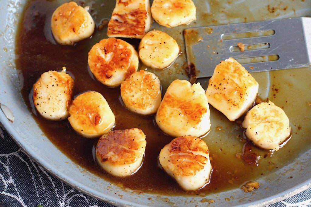 Glazed Pan Seared Scallops with Garlic and Honey in a pan with spatula