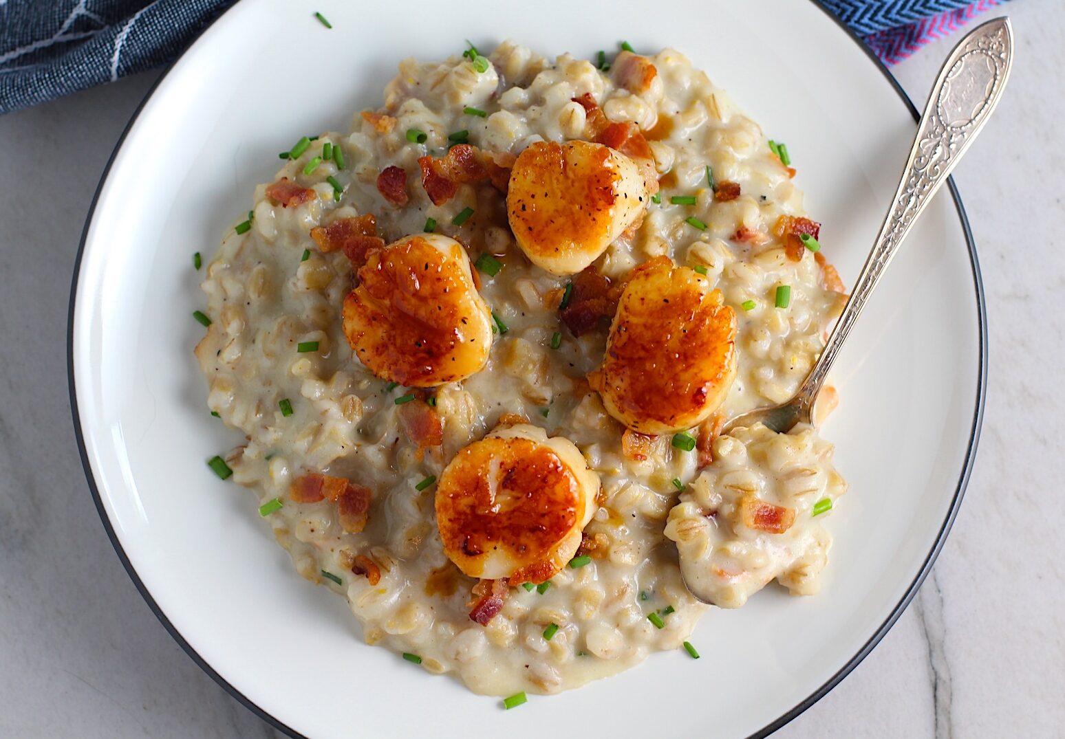 Glazed Pan Seared Scallops with Garlic and Honey sitting on Creamy Barley with Bacon bits and chives.