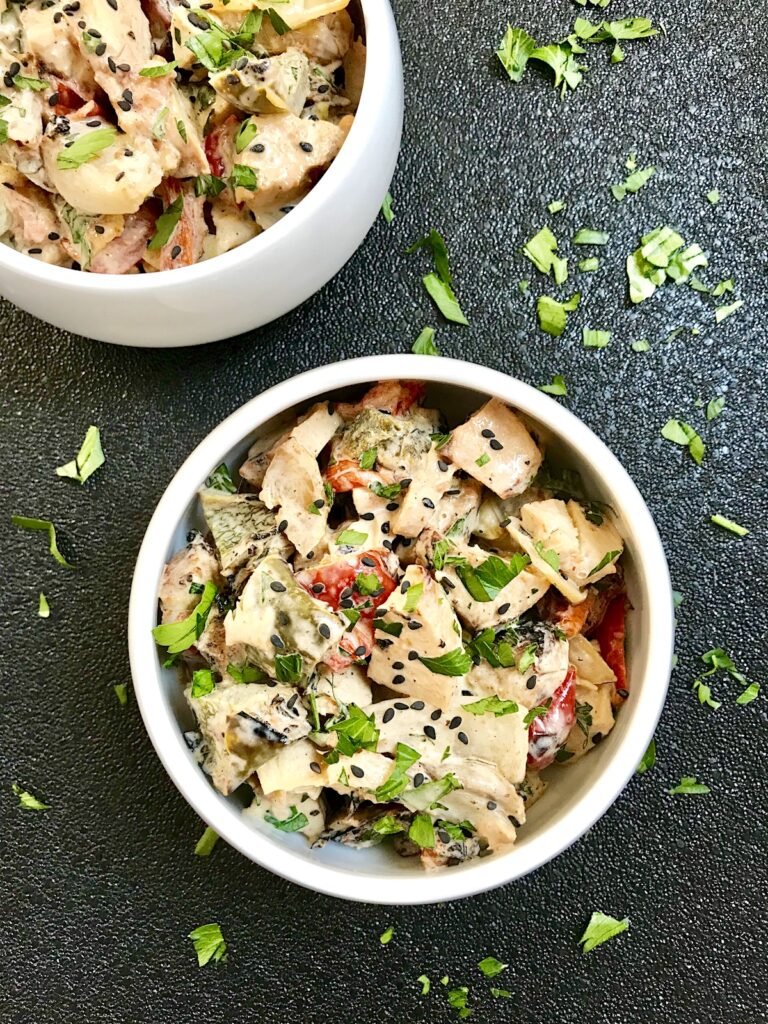 Grilled Teriyaki Chicken Salad in 2 bowls on black background with chicken, green peppers, tomatoes, onions, black sesame seeds, and cilantro.