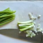 Scallion whites cut and separates from the greens with knife on cutting board for Dan Dan Noodle Recipe with Ground Chicken.