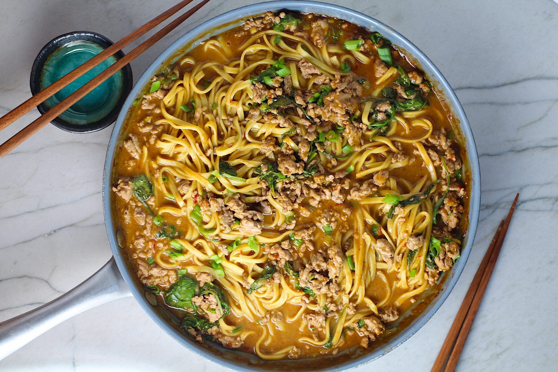 Dan Dan Noodle Recipe with Ground Chicken and scallions in a pan on counter with chopsticks next to it.