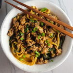 Dan Dan Noodle Recipe with Ground Chicken in a bowl. Chopsticks are sitting on top and scallion slices are on top.