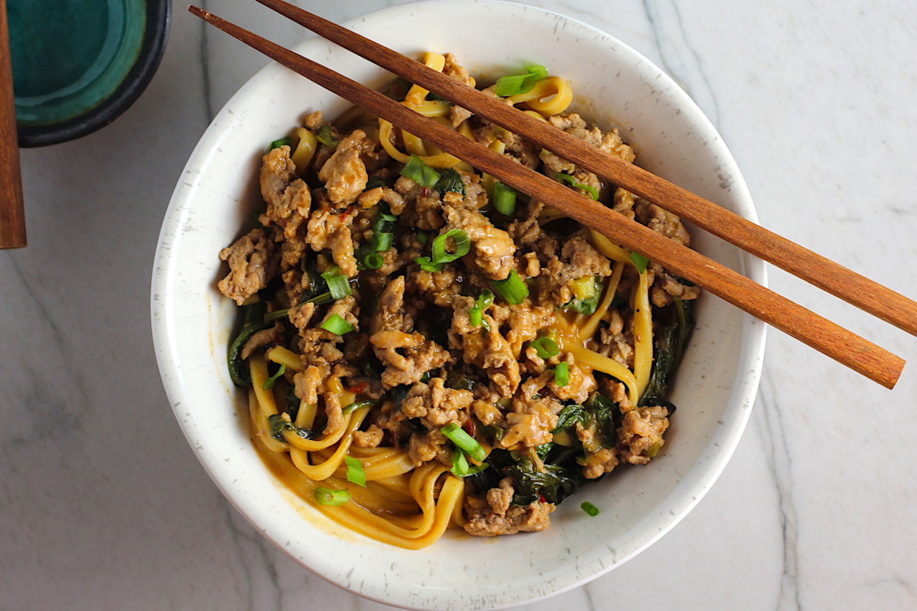 Dan Dan Noodle Recipe with Ground Chicken in a bowl. Chopsticks are sitting on top and scallion slices are on top.