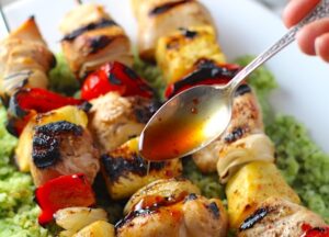 Spoon drizzling Sweet and Sour sauce over Chicken Kabobs with pineapple, onion, and red pepper over Green Rice with basil, chives, and spinach.