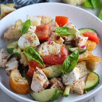 Toasted bread cubes, chicken, tomatoes, cucumber, basil, and mozzarella in a bowl for this Chicken Panzanella Salad Recipe. It's absolutely delicious.