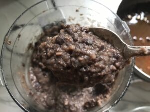 Spoon scooping pureed black beans over food processor for refried black beans recipe.