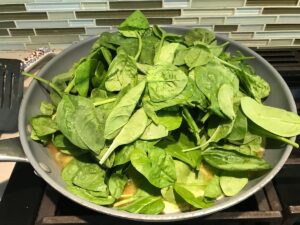 Fresh Baby spinach overflowing in a pan as it starts to cook into the Spinach Artichoke Chicken filling. It will be the stuffing into pitas.