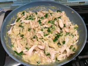 Spinach Artichoke Chicken filling in a large pan on stove for stuffing into pitas and then grilling.