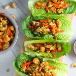 4 Cashew Chicken Lettuce Wraps on counter with a bowl of Cashew Chicken and Carrot filling on left and sauce on right.
