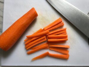 Carrot sticks cut on cutting board with knife for this Cashew Chicken Lettuce Wrap Recipe