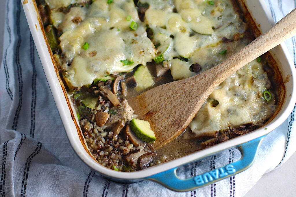 Chicken Wild Rice Casserole with Zucchini and Mushrooms in a casserole dish with missing corner piece and wood spatula in dish.