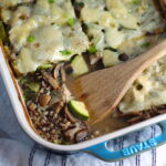 Chicken Wild Rice Casserole with Zucchini and Mushrooms in a casserole dish with missing corner piece and wood spatula in dish.