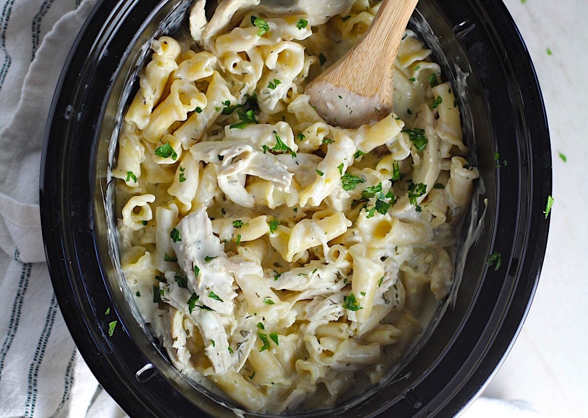 Ranch Chicken Crock Pot Pasta in the crockpot with wood spoon using fresh dill, parsley, and scallions is creamy, tangy, and utterly delicious! It's also so easy to make, so it's a great weeknight dinner.