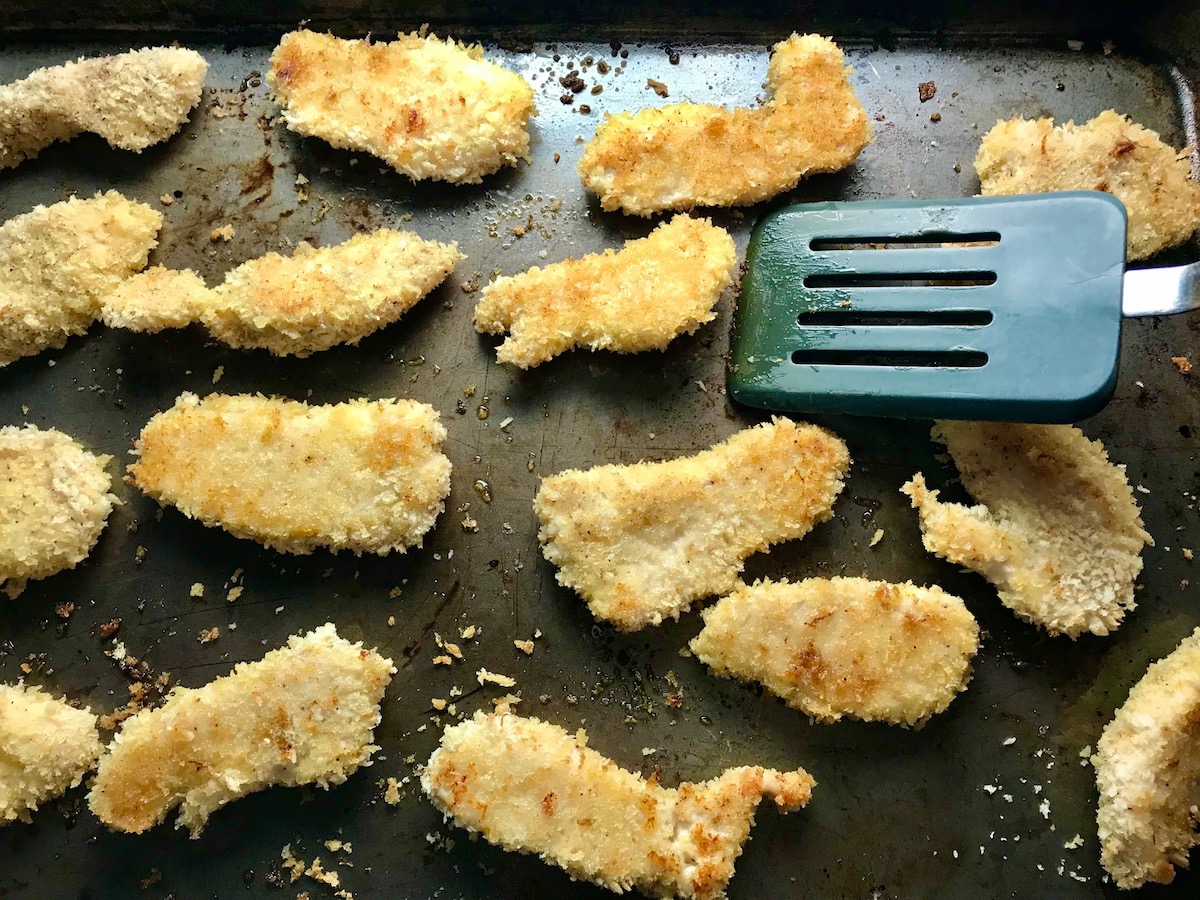 Cooked breaded chicken strips on a sheet pan for Kale Caesar Salad with Baked Crispy Lemon Chicken strips