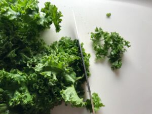 Knife cutting kale leaves into strips for Kale Caesar Salad with Baked Crispy Lemon Chicken strips